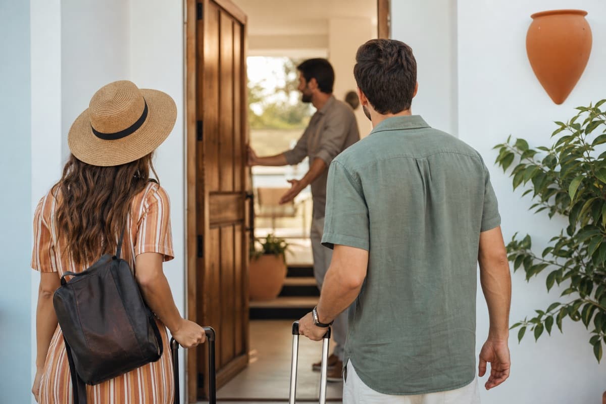 A host welcoming two guests with suitcases at the door of a holiday home